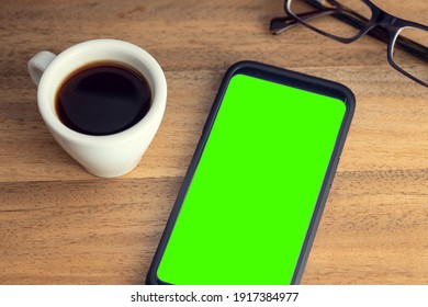 Smart phone on desk with green screen, eyeglasses and cup of coffee on wooden table. Mock up template. Chroma key - Powered by Shutterstock