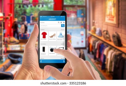 Smart Phone Online Shopping In Man Hand. Shopping Center In Background. Buy Clothes Shoes Accessories With E Commerce Web Site