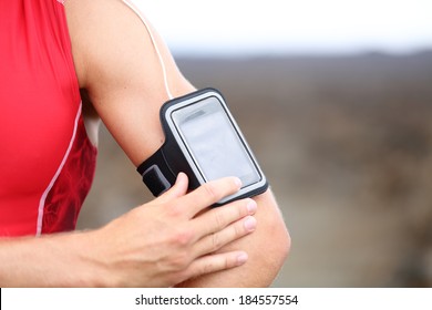 Smart phone running music closeup - male runner listening to music adjusting settings on armband for smartphone. Fit man fitness model working out outside in red sporty outfit. - Powered by Shutterstock