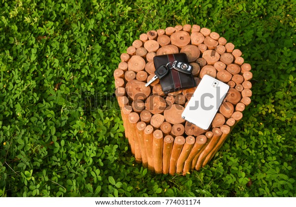 Smart phone, wallet and car key on a  seat or\
table made with logs of wood, Kerala India. Decorative rustic round\
wooden stool.\
