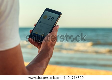 Smart phone with weather forecast on screen, smart phone dialing 29ºC at Matalascañas beach in Huelva, Andalusia, Spain