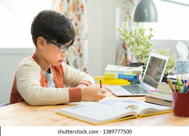 A smart preteen boy sitting at the table, writing homework or preparing for the exam. Teen using notebook computer to study. Student, School, Remote, Online learning, New normal, Home Based Learning. - Powered by Shutterstock