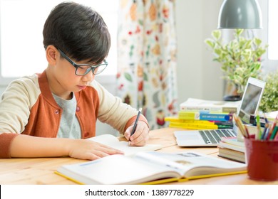 A smart preteen boy sitting at the table, writing homework or preparing for the exam. Teen using laptop to study. Online Education and learning for kids concept. - Powered by Shutterstock