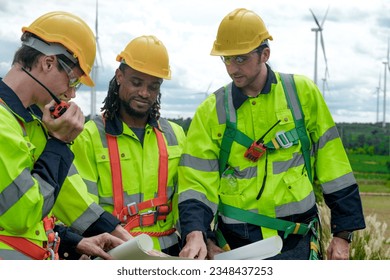 Smart professional engineers working in fieldwork outdoor. Workers meeting and celebrating at project site. Wind turbine electrical of clean resource energy and environment sustainable.