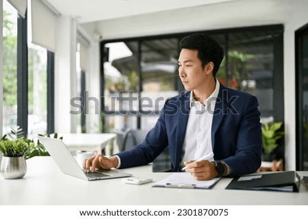 Smart and professional millennial Asian businessman or male boss focuses on his business tasks on laptop, working in his office.