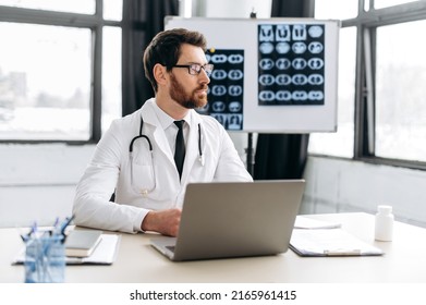 Smart proud focused caucasian male doctor of general medicine, dressed in a medical uniform and with glasses, sits at his workplace in a medical office, looks away, thinks about work