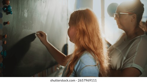 Smart Pupil Showcasing Math Knowledge: Static Shot of Elementary School Girl Solving Mathematical Problems Writing on the Chalkboard in Classroom. Female Teacher Checking Answers, Helping Student.