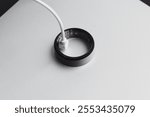 Smart ring is connected to a charging cable resting on a minimalist surface, illustrating advancements in wearable technology and modern design.