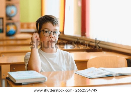 Smart schoolboy thinking about solving problem at school lesson, holding pencil near head and looking thoughtfully