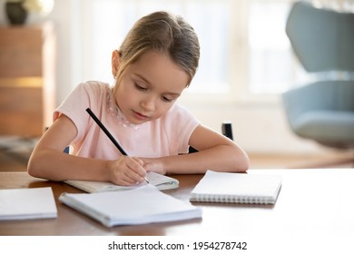 Smart small 7s Caucasian girl child sit at table at home write in exercise book prepare homework for school. Little kid handwrite in notebook do task assignment. Learning, education concept.