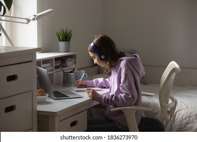 Smart Small Teenage Girl In Headphones Sit At Desk At Home Study Distant Online Using Modern Computer. Concentrated Teenager Pupil Prepare Homework Assignment On Laptop, Write Have Webcam Lesson.