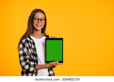 Smart smiling caucasian schoolgirl teenager child pupil student holding digital tablet showing blank screen with advert place mockup isolated in yellow background