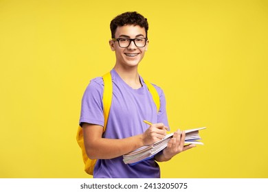 Smart smiling school boy wearing eyeglasses holding books taking notes isolated on yellow background. College student with backpack studying, learning language looking at camera. Education concept  - Powered by Shutterstock