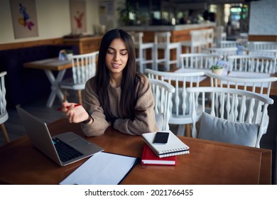 Smart South ASian Student Analyzing Education Information During Time For E Learning In Cafe Interior, Millennial Female Freelancer With Modern Laptop Computer Checking Notes From Paperwork