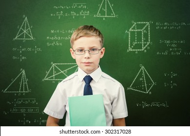 Smart student or schoolboy with a notebook, dressed in school uniform and sunglasses standing near blackboard scribbled with chalk - formulas and drawing. Concept of intelligent and scientist boy - Powered by Shutterstock