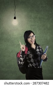 Smart student standing in the class and pointing at a bright light bulb