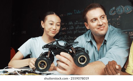 Smart teacher inspect car model construction to diverse student. Highschool children with mixed races listening mentor explain robotic model system at table with laptop and wires placed. Edification. - Powered by Shutterstock