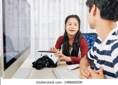 Smart teenage girl explaining idea for video game for virtual reality headset to her friend when they are sitting at desk with cimputer