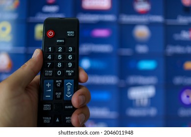 Smart tv and hand pressing remote control. Hand holding TV remote control with a television in the background. Close up.