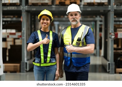 Smart warehouse worker wearing uniform with reflective jacket and helmet in distribution store, show thumb up for mission success. Coworkers collaborate together to deliver shipment, logistic business - Powered by Shutterstock