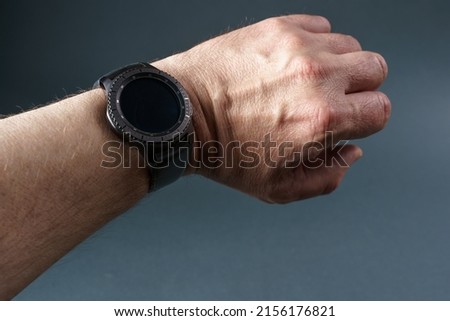 Smart watch with a black screen on a man's hand, close-up on a gray background.