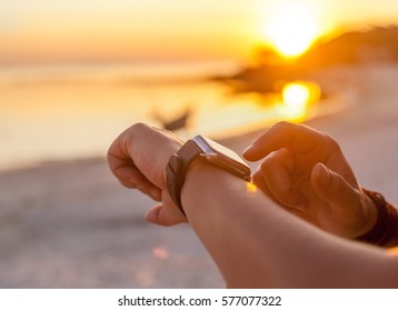 Smart watch woman using smartwatch touching button and touchscreen on active sports activity or morning jogging during beach sunrise or sunset. Closeup of hands and wrist with smart watch screen.