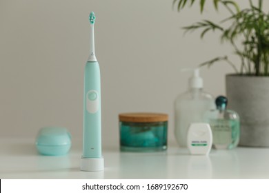 Smart wireless ultrasonic toothbrush standing on charger in light bathroom. Innovative oral care technology. Beautiful blue color women's set. Concept of modern healthcare.