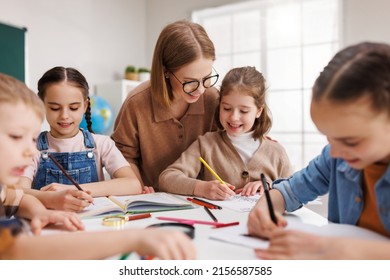 Smart woman in casual clothes and glasses helping students to to schoolwork during lesson in light classroom at school - Shutterstock ID 2156587585