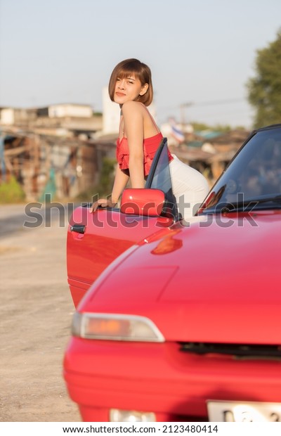 A smart woman model take a picture and\
post acting with red car is classic car and open roof , The red car\
is accumulate for some people like\
it