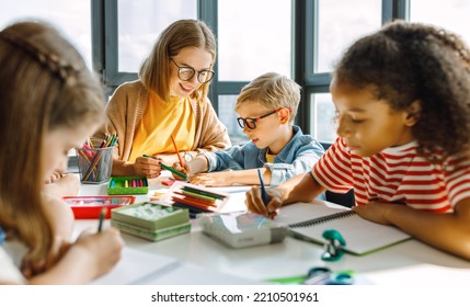 Smart woman teacher in  glasses helping students to to schoolwork during lesson in light classroom at school