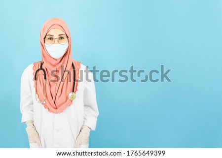 Smart young asian muslim woman doctor in lab coat with Medical face mask,white latex medical gloves and stethoscope against blue background,health care concept
