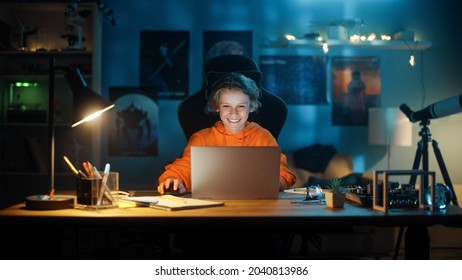 Smart Young Boy Using Laptop Computer In A Dark Cozy Room At Home. Happy Teenager Browsing Educational Research Online, Chatting With Friends, Studying School Homework.