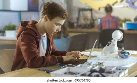 Smart Young Boy Works on a Laptop For His New Project in His Computer Science Class. Other Children Learning in the Background. - Powered by Shutterstock