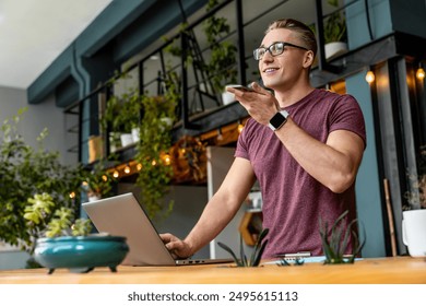 Smart young caucasian business man freelancer it worker guy manager male student recording voice message talking on mobile smart phone with customers partners while working studding in office cafe