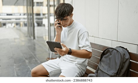 Smart young hispanic teenager, a university student, deeply engrossed in a serious phone conversation using his smartphone and touchpad, casually sitting outdoors on campus. - Powered by Shutterstock