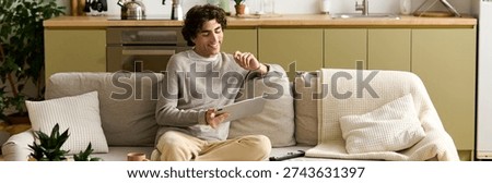 Smartly dressed young man spends leisure time at home, smiling and engaging with a tablet, banner 