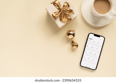 smartphone with 2024 calendar open on it, cup of coffee, gift box and Christmas balls on the table, top view. New Year's Eve planning - Powered by Shutterstock