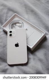 Smartphone Apple IPhone 12 White With A Box Picture Taken On A Bed Inside A Room On The Day Of Purchase. Omsk, Russia 18 June 2021. 