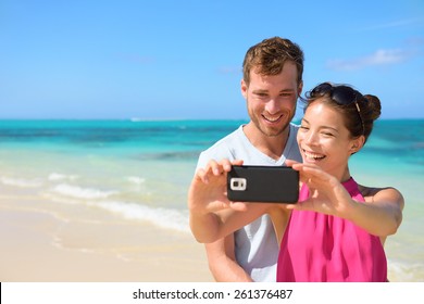 Smartphone - beach vacation couple taking selfie photograph using smartphone relaxing and having fun holding smart phone camera. Young beautiful multicultural Asian Caucasian couple on summer beach. - Powered by Shutterstock
