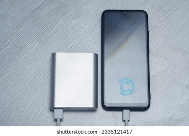 The smartphone is being charged using a portable charger on a wooden table