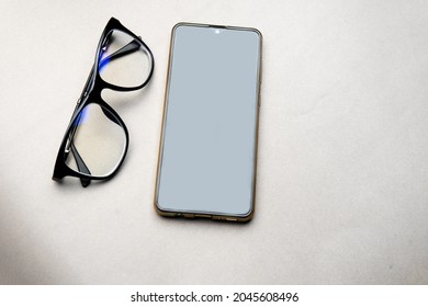 Smartphone And Black Frame Blue Light Blocking Technology 
 Anti Glare Spectacles Glasses On Grey Background