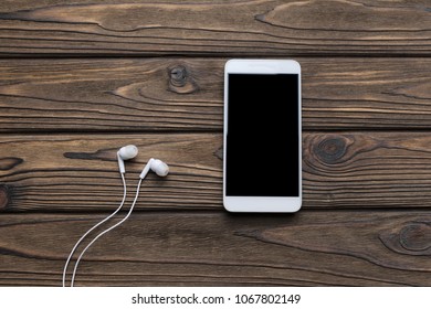 smartphone with black screen, headphones on the background of a wooden table. internet, listening to music. - Powered by Shutterstock