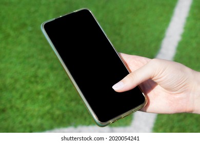 Smartphone with black screen in woman hand against the soccer field. Using mobile apps for workouts and at sports events. Copy space - Powered by Shutterstock