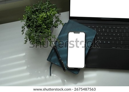 Smartphone with blank screen on notebook, and laptop, with plant decor on desk