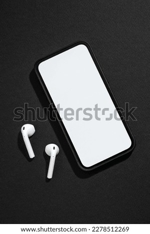Smartphone with blank screen and wireless headphones next to it on dark gray background