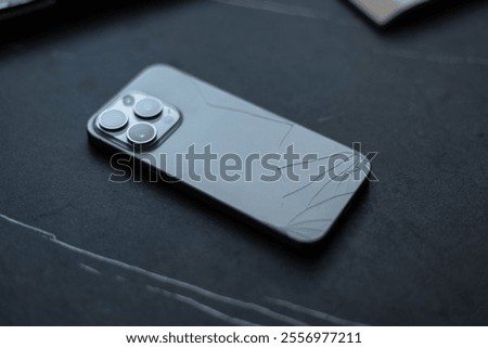Smartphone with a broken back panel with cracks on a black background. The phone fell and broke
