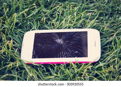 Smartphone with broken screen lying on green grass