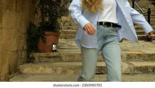 Smartphone with camera app running timer stand on stairs in antique street. Anonymous woman start shutter countdown on phone and run to shoot place to take selfie in touristic place.
