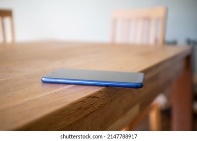 Smartphone is carelessly left on the edge of a wooden table and can fall. Concept of careless attitude to things.