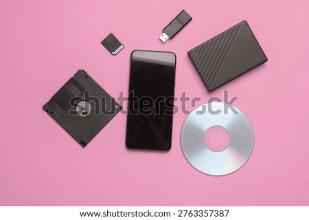 Smartphone with CD disk, floppy disk, USB flash drive, sd card and external hard drive on pink background. Digital information media. Flat lay